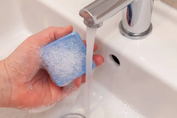 Holding a blue bar of soap under a running tap in a bathroom sink. Medical cleanliness concept