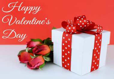 Beyaz, kare hediye kutusu kırmızı arka plan beyaz masada kırmızı ve beyaz puantiyeli kurdele ile süslenmiş. İpek kırmızı gül yanındaki kutuyu döşeme. Sevgililer mesaj eklendi