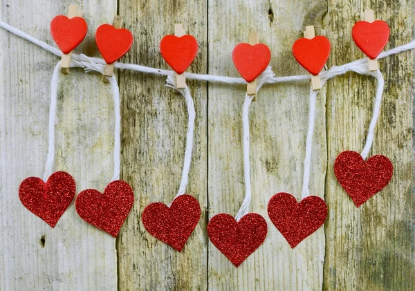 Sparkly red hearts handing from decorated clothespins by string in front of rustic wooden background for Valentines Day.