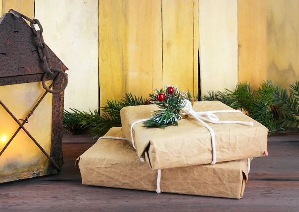 Kırsal bir fener, içinde parlayan bir mum olan ahşap bir masa ve Aralık ayında Noel hediyesi olarak kahverengi bir kağıda sarılmış. Boşluğu kopyala.