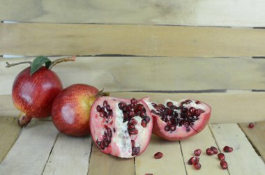 Taze bir pompegranat açık, bütün sulu kırmızı tohumları gösteriyor, tahta zemin ile tahta kesme tahtasında iki tam meyve var.