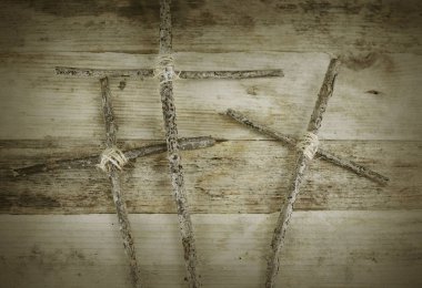 Three handmade crosses lashed together with twine on a rustic wooden background. The crosses represent the crucifixion of Jesus Christ. Vignetter and vintage filter added