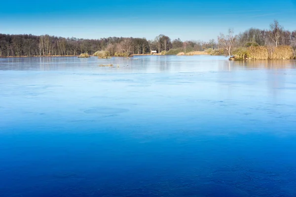 Gelo no lago por dia ensolarado. Grande superfície azul com árvores e re — Fotografia de Stock