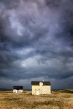 Old abandoned fishermans cottage and outbuilding with dramatic storm clouds, Canada  clipart