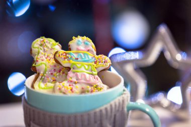 Masada zencefilli kurabiyelerle dolu bir kupa ve arka planda Noel ağacı ışığı.