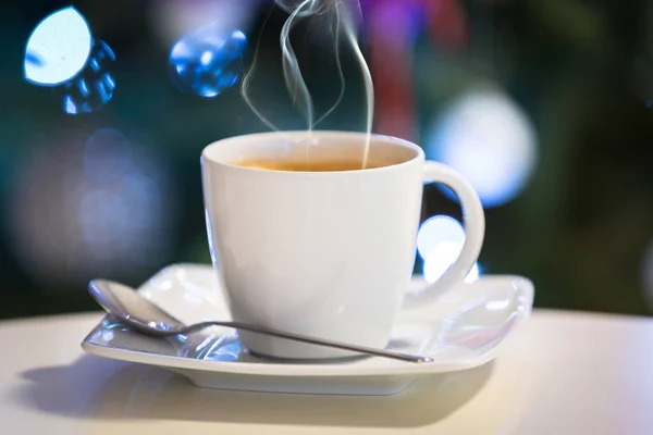 Xícara de café quente a mesa com luzes de árvore de natal na parte de trás — Fotografia de Stock