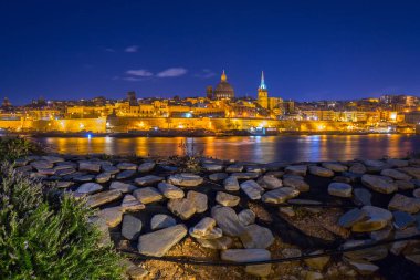 Malta 'nın Rocky sahili ve Valletta şehrinin geceleri mimarisi.