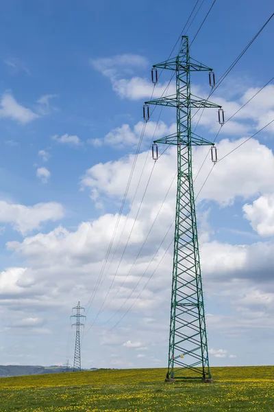 Linie wysokiego napięcia powyżej wiosenna łąka. Słupach elektrycznych — Zdjęcie stockowe