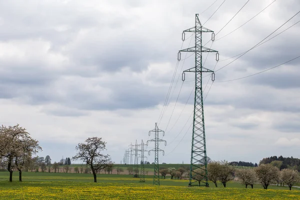 Hochspannungsleitungen über der Frühlingswiese. Strommasten — Stockfoto