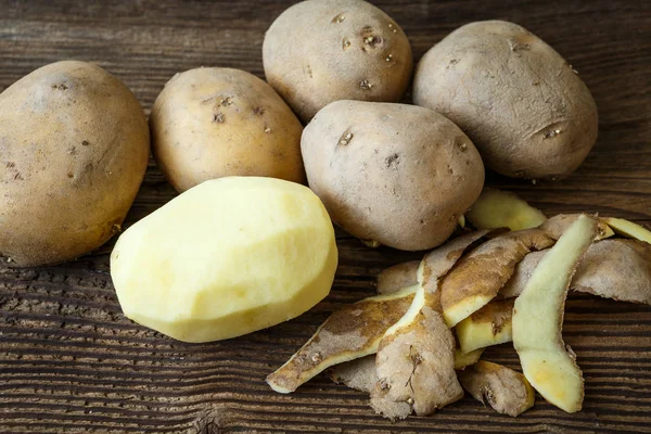 Batata descascada e pilha de batatas na mesa de madeira rústica — Fotografia de Stock