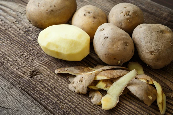 Batata descascada e pilha de batatas na mesa de madeira rústica — Fotografia de Stock
