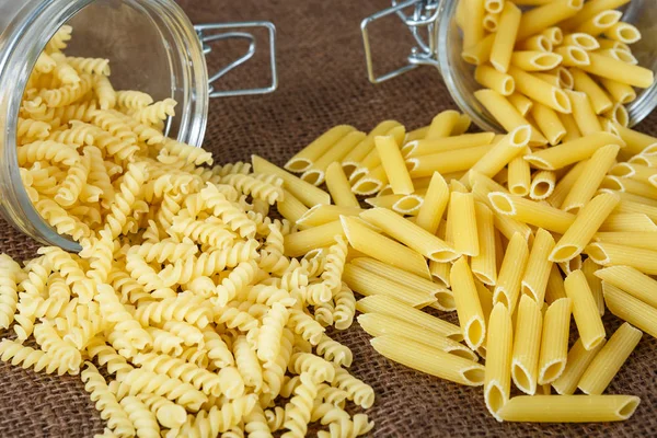 Włoski makaron - penne i fusilli w szklanym słoju na brązowy backgrou — Zdjęcie stockowe