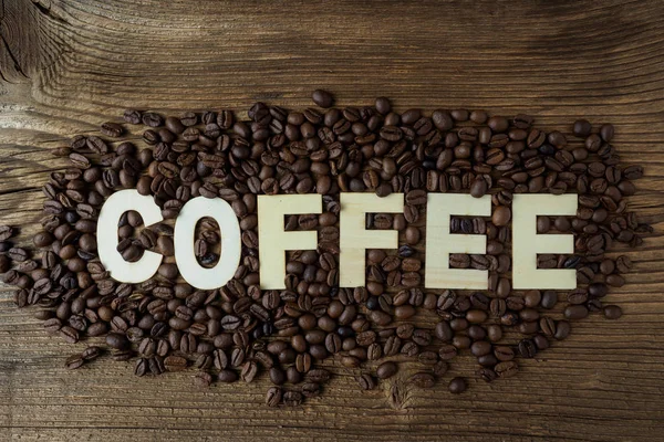 Schwarze Kaffeekörner liegen auf einem braunen Holztisch. — Stockfoto