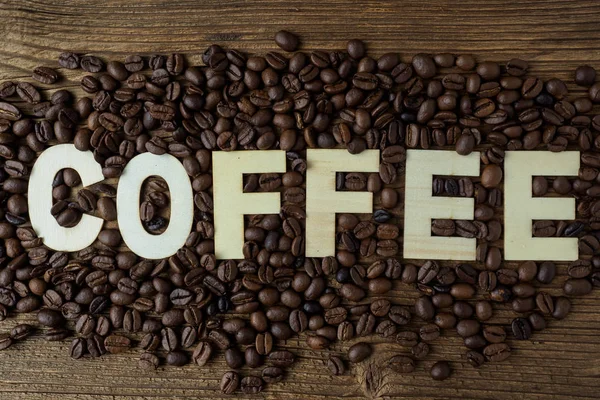 Schwarze Kaffeekörner liegen auf einem braunen Holztisch. — Stockfoto