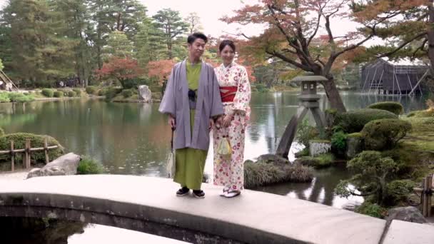 Japanska bröllop par i traditionell kimono stå på en bro i Kenrokuen park, Kanazawa stad, Japan — Stockvideo