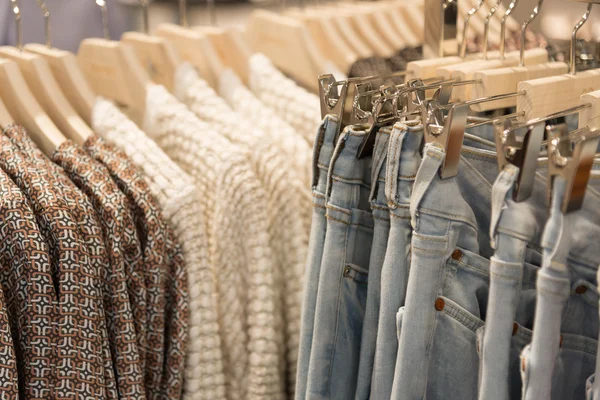 Womens clothes and jeans are hanging on hangers in store — Stock Photo, Image