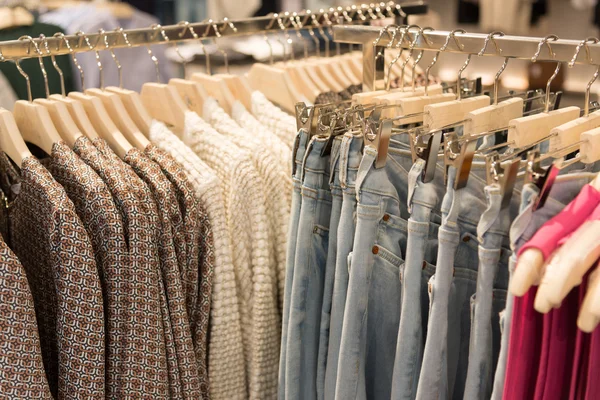 Womens clothes and jeans are hanging on hangers in store — Stock Photo, Image