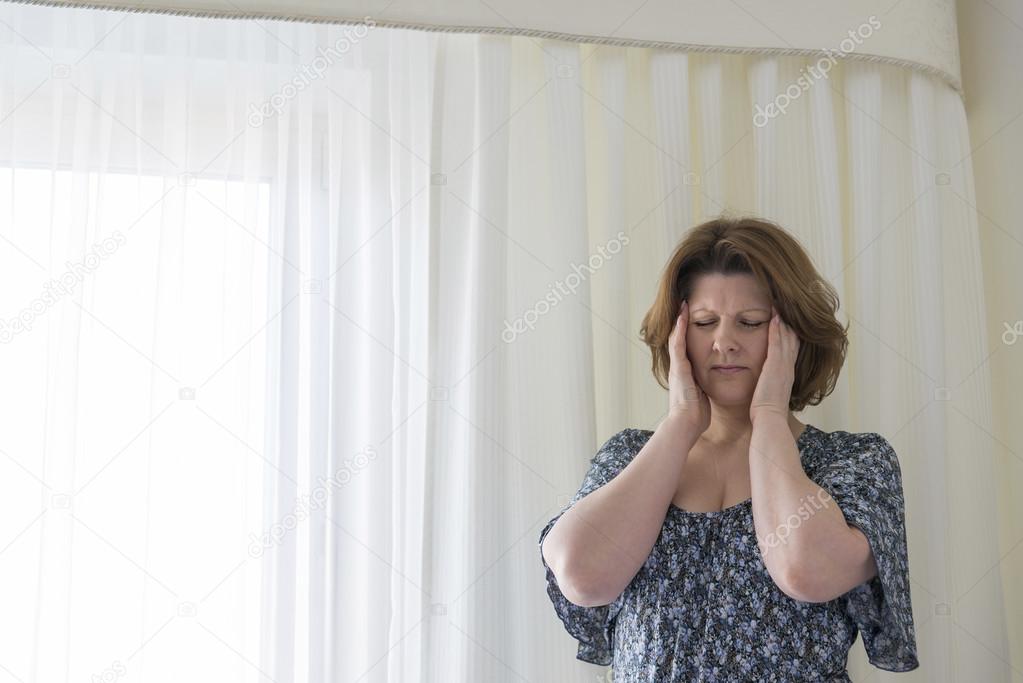 woman tired to hang curtains and experiencing headache