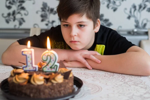 Tiener jongen kijkt peinzend taart met kaarsen op de twaalfde dag van de geboorte — Stockfoto