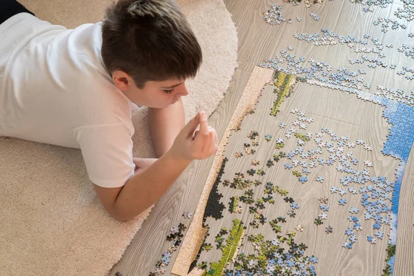 Хлопчик-підліток збирає головоломку, що лежить на килимі — стокове фото