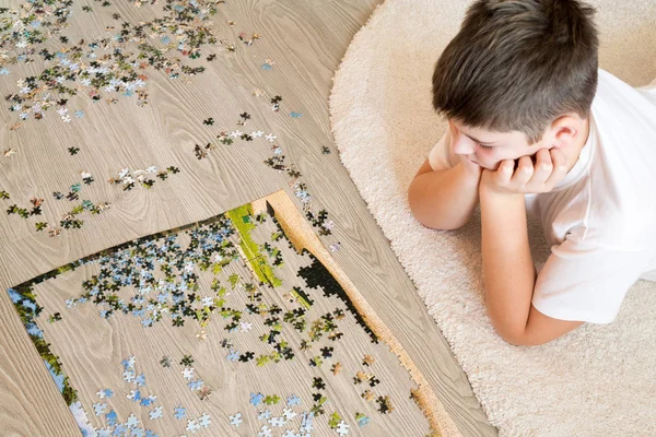 Teen boy collects a puzzle lying on carpet — Stock Photo, Image