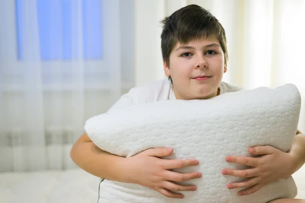 Der Junge hält das anatomische Kissen in der Hand, das auf dem Bett sitzt — Stockfoto