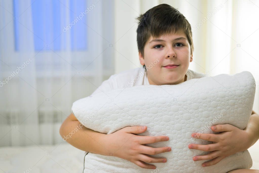The boy holds in his hands the anatomical pillow sitting on bed