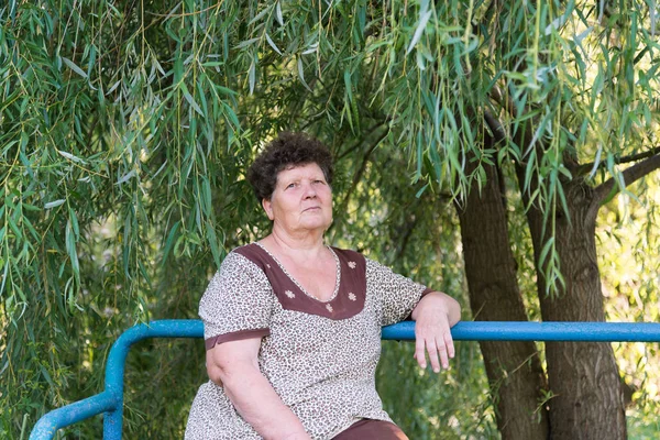 Érett nő ül a padon szomorúfűz göndör haja — Stock Fotó