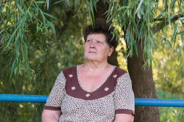 Starsza kobieta siedzi na ławce wierzby — Zdjęcie stockowe