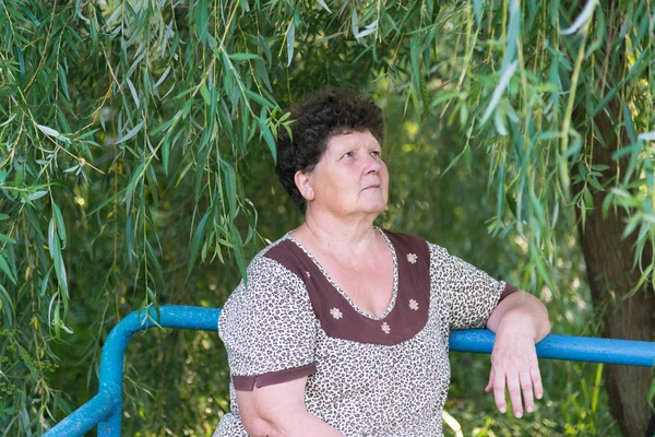 Mogen kvinna sitter på en bänk weeping willow — Stockfoto