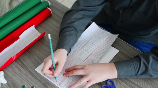 Хлопчик-підліток малює деталі для різдвяної листівки з кольорових самоклеючих паперів — стокове відео