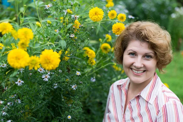 Uśmiechnięta kobieta w pobliżu żółte kwiaty w przyrodzie — Zdjęcie stockowe