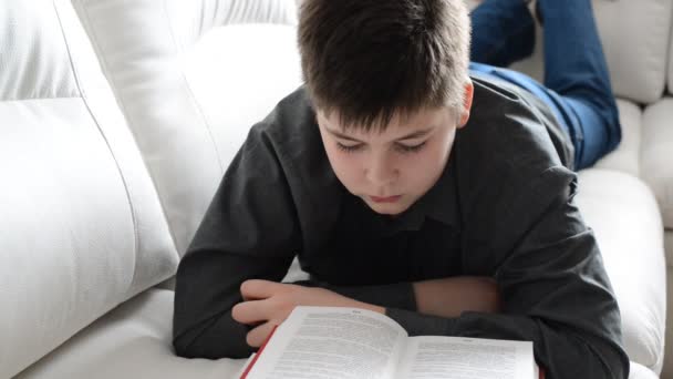 Adolescente lendo um livro deitado no sofá no quarto . — Vídeo de Stock