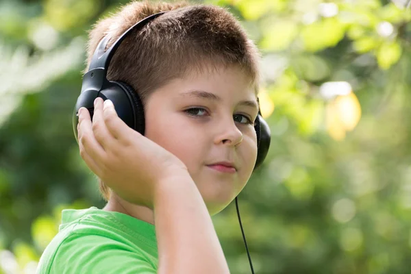 Niño escuchando música con auriculares en el parque — Foto de Stock