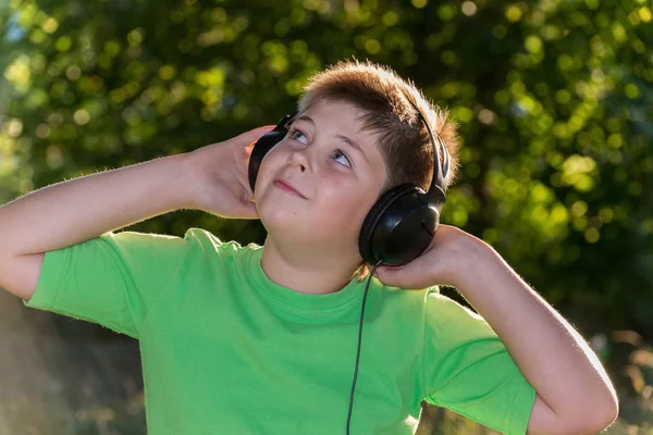 Chico alegre escuchando música con auriculares en el parque — Foto de Stock