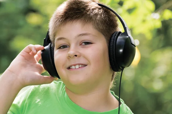 Neşeli çocuk parkta kulaklıkla müzik dinliyor — Stok fotoğraf