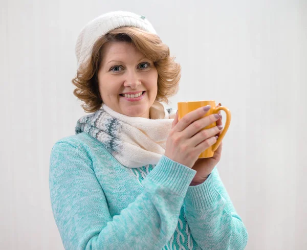 Жінка в светрі, капелюсі і шарфі тримає жовту чашку чаю — стокове фото
