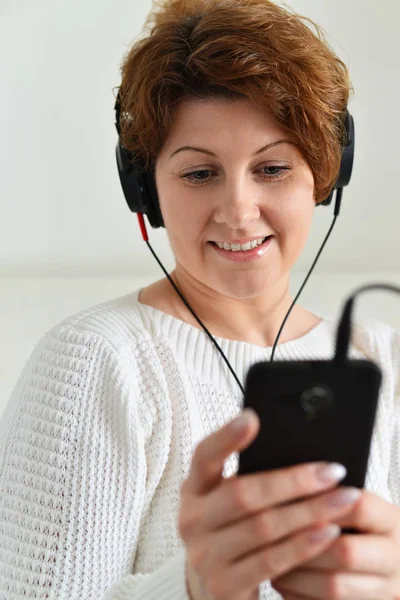 Mulher em fones de ouvido olha para smartphone — Fotografia de Stock