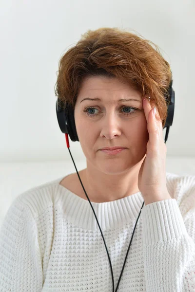 Mulher em fones de ouvido com dor de cabeça — Fotografia de Stock
