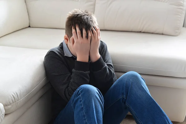 Enojado adolescente 13 años, él se sienta cerca del sofá cubriendo su cara con sus manos — Foto de Stock