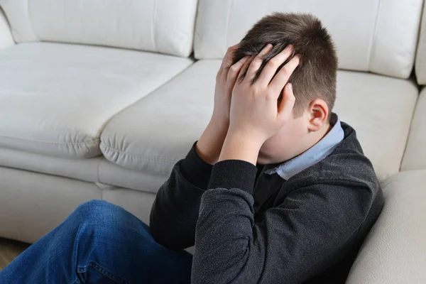 Sconvolto adolescente 13 anni, si siede vicino al divano coprendole il viso con le mani — Foto Stock