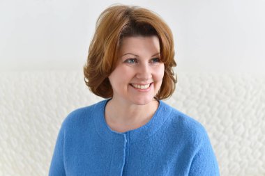 Kanepede oturan ve uzağa bakarak gülümseyen kadın