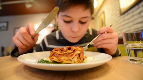 Мальчик ест лазанью в кафе — стоковое видео