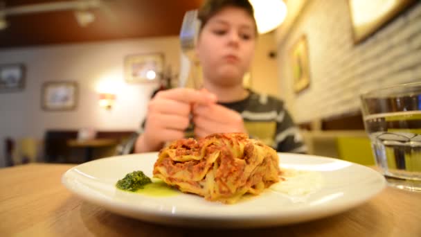 Chłopiec jest jedzenie lasagne w kawiarni z noża i widelca — Wideo stockowe