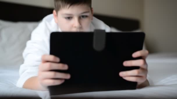 Teenager in white bathrobe on bed and playing on tablet — Stock Video