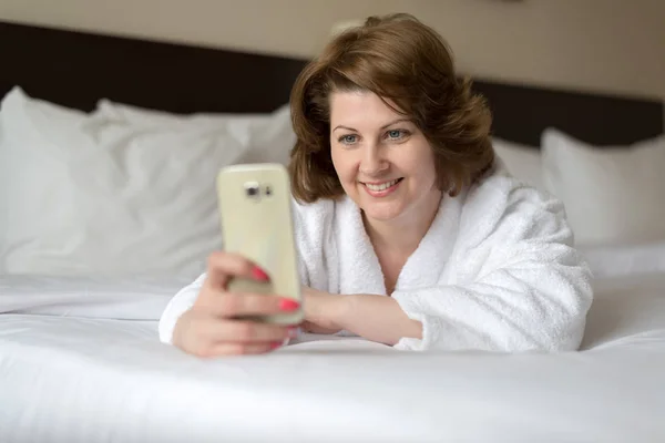 Fürdőköpeny egy nő visel telefon szállodai szobában — Stock Fotó