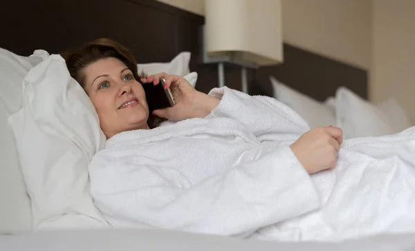 Жінка в халаті розмовляє по телефону в готельному номері — стокове фото
