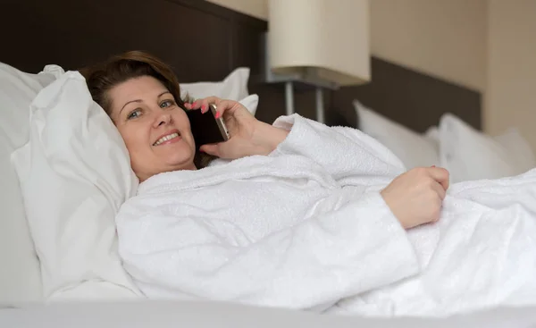 Жінка в халаті розмовляє по телефону в готельному номері — стокове фото