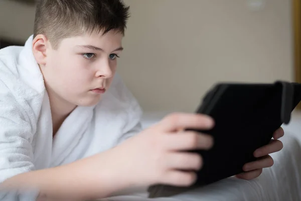 Niño en albornoz Utiliza tableta en la habitación del hotel — Foto de Stock