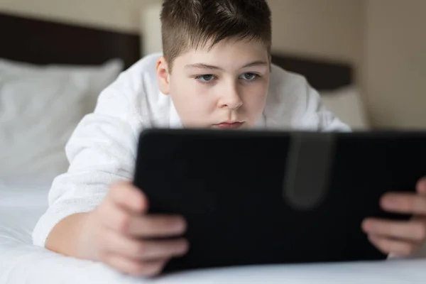 Niño en albornoz Utiliza tableta en la habitación del hotel — Foto de Stock